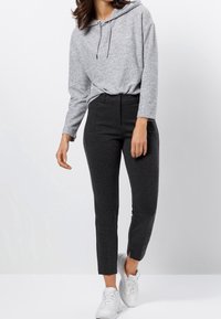 Haut à capuche gris avec cordons, associé à un pantalon gris foncé fuselé avec poches et ourlets fendus, complété par des baskets blanches.