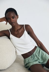 Camisole blanche à côtes avec des bords festonnés, associé à un short en satin vert clair avec une taille élastique et un cordon de serrage.