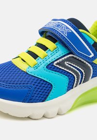 Baskets bleues avec tige en mesh, lacets jaunes et accents verts. Dotées d'une semelle rembourrée et d'une sangle en velcro avec un détail de logo.