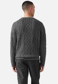 Suéter gris de punto con patrón de cable, dobladillo acanalado y mangas largas, combinado con pantalones gris oscuro, visto desde la espalda.
