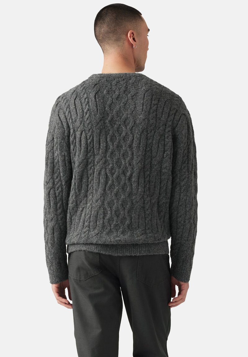 Suéter gris de punto con patrón de cable, dobladillo acanalado y mangas largas, combinado con pantalones gris oscuro, visto desde la espalda.