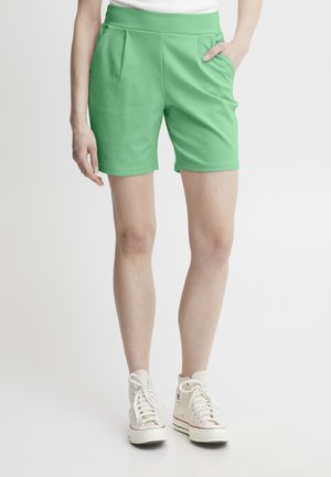Gröna shorts med en slät yta, utrustade med två sidoblock och ett högt, elastiskt midjeband. Bärs med beiga högskor.