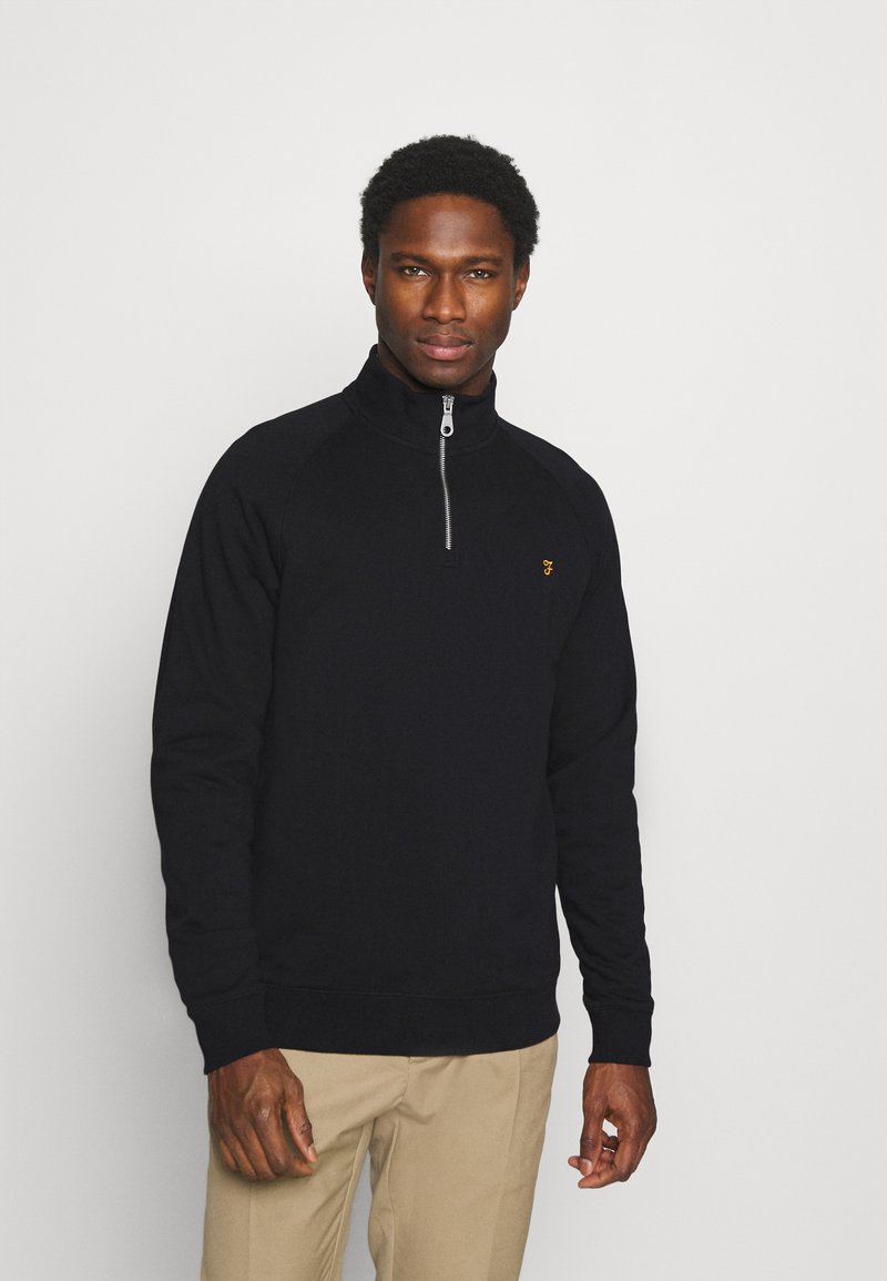 Black zip-neck sweatshirt featuring a ribbed collar and cuffs, made from textured fabric, with a small gold logo on the chest.