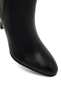 Botte de cheville en cuir noir avec un bout pointu, texture lisse et un talon bloc modeste. Le design présente des détails minimalistes.