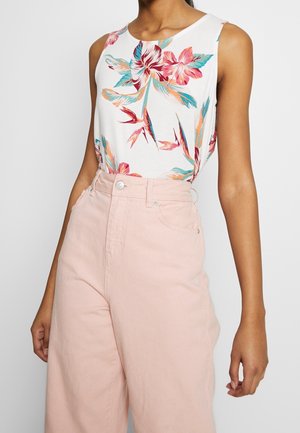 Haut blanc sans manches avec imprimé floral coloré, associé à un pantalon taille haute à jambes larges de couleur rose pâle porté par une personne.