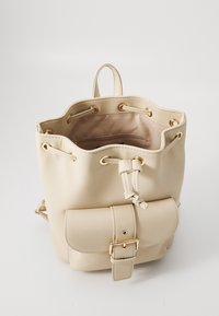 Sac seau beige en simili cuir avec quincaillerie dorée, fermeture à cordon, et une poche avant sécurisée par une boucle. Fini texturé.