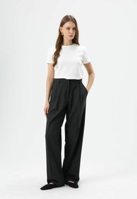 Witte kortermige blouse gecombineerd met hooggetailleerde, losvallende donkergrijze broek. Soepele stof met een gestructureerd ontwerp, zonder zichtbare patronen.