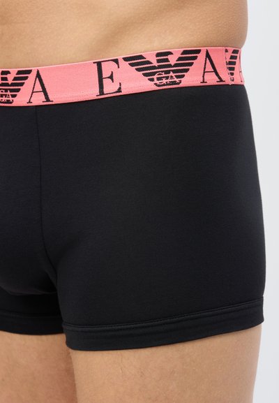 Μαύρο μπόξερ σλιπ με ροζ ελαστική μέση, διακοσμημένο με μαύρα λογότυπα και γράμματα αετού Emporio Armani, φορεμένο σε άνδρας στο ισχίο και το μηρό.