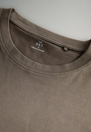 Brun bomulds t-shirt med rund hals, blød tekstur og syningsdetaljer. Etiketten siger "THE SET M MADE IN BANGLADESH" på indersiden af halsen.