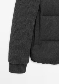 Dark gray knitted sleeve with ribbed cuff next to a padded jacket section with a horizontal seam and pocket opening.