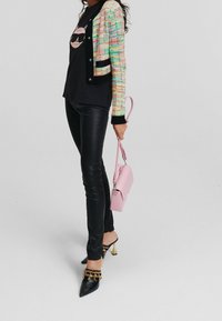 Cardigan in tweed multicolore, t-shirt nero con grafica, pantaloni neri in ecopelle, mules nere con accenti dorati, borsa rosa.