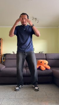 Person in a navy t-shirt and dark jeans stands in a living room. A plush orange octopus toy with purple accents sits on a gray sofa.