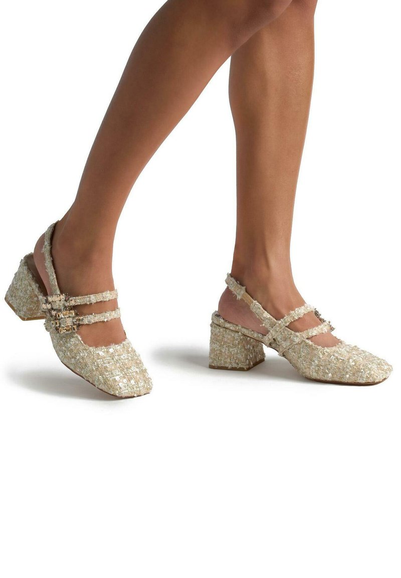 Scarpe in tessuto beige, con texture, punta quadrata, cinturini alla caviglia e tacco chunky. Presentano due fibbie decorative sui cinturini.