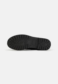 Semelle en caoutchouc noir présentant des motifs de crampons profonds et un insert rectangulaire, conçue pour l'adhérence et la durabilité.