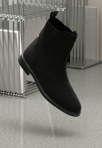 Stivaletto nero con superficie liscia, pannelli laterali elastici e tacco basso. Presenta una punta arrotondata e un sottile dettaglio di branding.