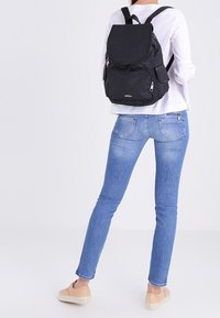 Czarny plecak z teksturowaną powierzchnią, przednią kieszenią na zamek i bocznymi kieszeniami. Wzór posiada regulowane ramiączka oraz zaokrągloną klapkę zamykającą.