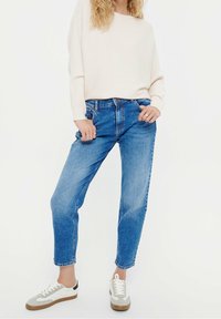 Vaaleanbeige ribbineulepaita yhdistettynä klassisiin sinisiin suoraan lahkeeseen leikattuihin farkkuihin. Jalkineissa valkoisia, harmaita ja mustia yksityiskohtia. Sileät kangaspinnat.