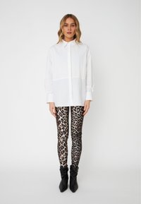 Hvit skjorte med vertikale folder, kombinert med tettsittende svarte og beige leopardmønstrede leggings og svarte spisse ankelstøvler.