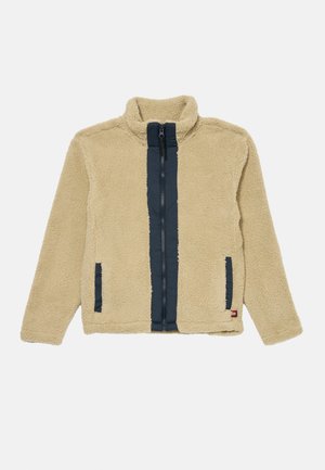 Giacca in fleece beige con pannello frontale blu navy; presenta una chiusura con zip e due tasche laterali. Materiale morbido e design con alto colletto.