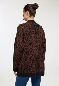 Brązowy i czarny sweter o dużym rozmiarze w paski jak u tygrysa, o luźnym kroju, ściągaczach na rękawach i zaokrąglonym dolnym wykończeniu. Teksturowana tkanina dodaje głębi.
