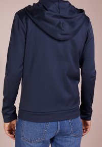 Navy Kapuzenpullover mit einer strukturierten Oberfläche und gerippten Bündchen, bietet eine klassische Passform und eine Kängurutasche, kombiniert mit blauen Jeans.