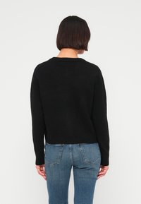 Μαύρο πλεκτό πουλόβερ με στρογγυλή λαιμόκοψη, πέτα ώμους και κοντό τελείωμα. Συνδυασμένο με ανοιχτό μπλε, εφαρμοστά τζιν παντελόνια.