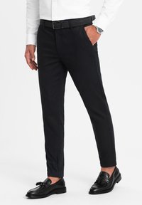 Pantaloni neri, sartoriali, con una vestibilità slim, dotati di tasche laterali e una cintura nera strutturata. Indossati con mocassini neri lucidi.