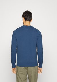 Sweater azul marinho com mangas longas, punhos e barra canelados; apresenta um pequeno detalhe riscado na parte de trás do pescoço.