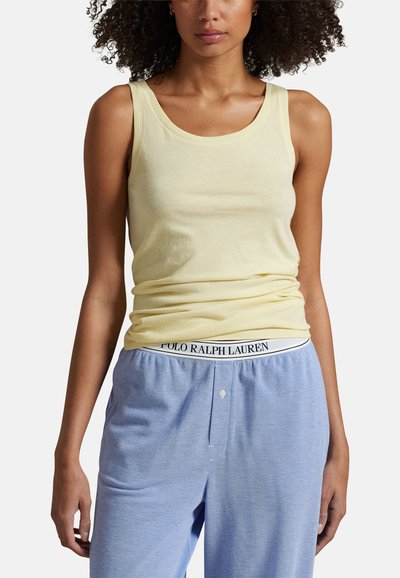 Femme portant un débardeur sans manches jaune clair et un pantalon bleu clair avec une ceinture visible Polo Ralph Lauren.