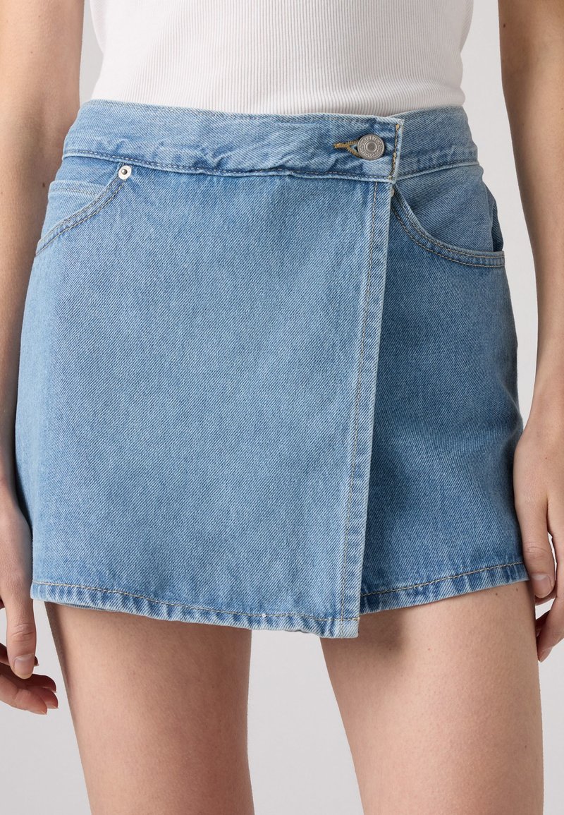 Denim-Minirock in Hellblau mit rohem Saum, seitlichen Taschen und einer vorderen Knopfleiste. Weicher, strukturierten Stoff mit sichtbaren Nähten.