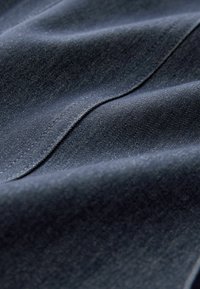 Tume teksariie kangas on sileda tekstuuriga, kergelt läikiva pinnaga, esitades rikkalikku mereväe sinist värvi ja peent diagonaalset põimitud mustrit.