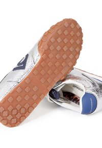 Zapatillas metálicas plateadas con acentos azules, parte superior texturizada, forro blanco y suela de goma marrón con un patrón de diamantes.