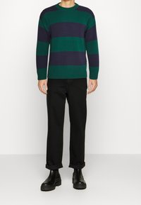 Pull rayé vert et bleu marine avec poignets et ourlet côtelés, associé à un pantalon noir retroussé et des bottes noires épaisses.