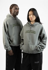 Felpe grigie con zip e cappuccio hanno una vestibilità rilassata, polsini elasticizzati e coulisse. Logo "WASTED" in verde sul petto. Pantaloni sudati neri con logo laterale.