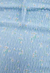 Tessuto blu chiaro con texture e piccoli motivi floreali in bianco e verde. La superficie appare arricciata e morbida, evidenziando un design delicato.