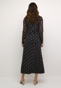 Črna maksi obleka s prozornimi dolgimi rokavi, ki prikazuje vzorec v beli barvi. Gladek material z udobnim krojem in dolžino do tal.