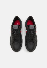 Pár černých tenisek Tommy Hilfiger s červenými a bílými postranními pruhy, černými tkaničkami a červenými polstrovanými vložkami, zobrazených shora.