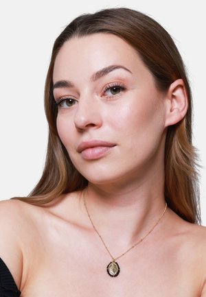 Collier pendentif en or présentant une forme ovale avec des accents noirs, exposé sur un cou nu. Texture douce et détails de chaîne fins.