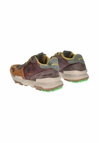 Sneaker atletiche marroni e grigie con una suola grigia punteggiata e tacchetti verdi. Presentano una combinazione di suede e pelle testurizzati con accenti gialli.