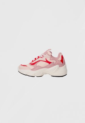 Baskets FILA roses et rouges avec des lacets blancs et une épaisse semelle blanche, présentées de côté sur un fond gris clair uni.
