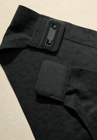Black garment featuring textured fabric with adjustable hardware. Includes a smooth panel and stitching details for fit and support.