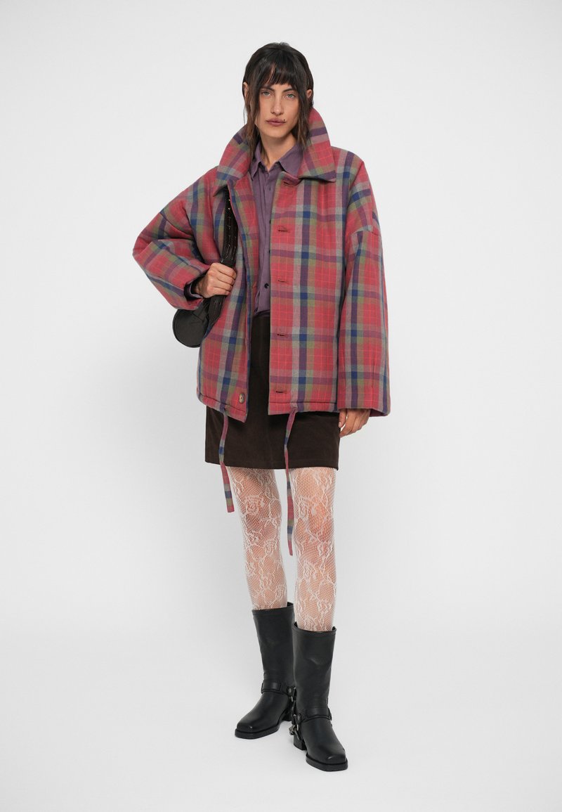 Plaid jacket in pink, blue, and green tones with a boxy fit, large collar, and button closure. Worn over a purple shirt and brown skirt.