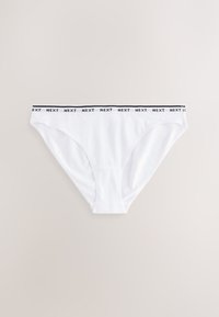 Sous-vêtement style bikini blanc avec taille élastique noire affichant le texte répété « NEXT », posé à plat sur une surface claire.