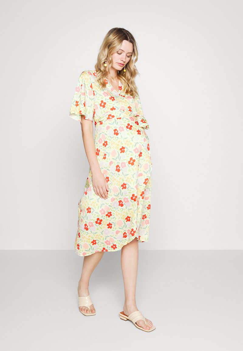 Vestido midi floral em amarelo claro, com mangas curtas e um laço na cintura. Os padrões incluem flores vermelhas e cor-de-rosa com folhas verdes.