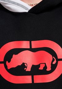Zwarte hoodie met een grote rode neushoornsilhouet binnen een afgerond rechthoek, die contrasteert met een witte lijn bij de capuchon.