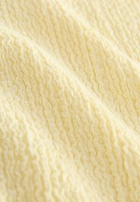 Tissu jaune pâle doux avec une texture côtelée formant de douces plis et un motif ondulé.