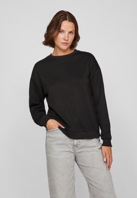 Felpa nera con maniche lunghe, collo a giro, polsini e orlo a costine. Jeans grigi chiari, dal taglio ampio. Design semplice, senza motivi.