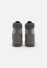 Cizme gri de tip mid-top cu finisaj texturat, având un guler căptușit gri, talpă robustă și spate întărit pentru durabilitate.
