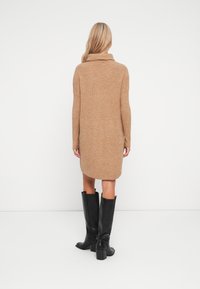 Langsleeve, geribbelde jurk in de kleur camel met een colsjaal. Gepaard met zwarte leren laarzen tot de knie met een blokhak.