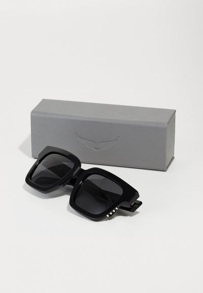Occhiali da sole neri oversize con lenti scure, montatura quadrata, finitura lucida e tre borchie decorative sulla stanghetta. Include una scatola grigia.